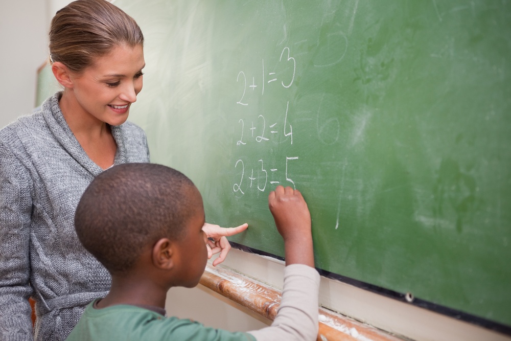 Cute teacher and a pupil making an addition on a blackboard